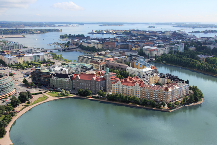 Aerial view of Helsinki Congress Paasitorni, surrounded by water, colorful buildings, and cityscape under a clear blue sky.