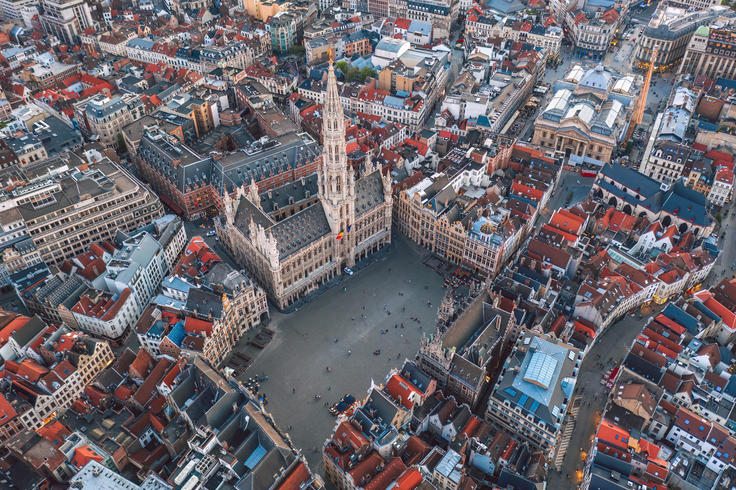 Aerial view of a historic city square surrounded by ornate buildings with a tall spire in the center.