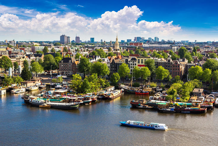 Canal view of a city with boats and green trees under a blue sky with clouds.