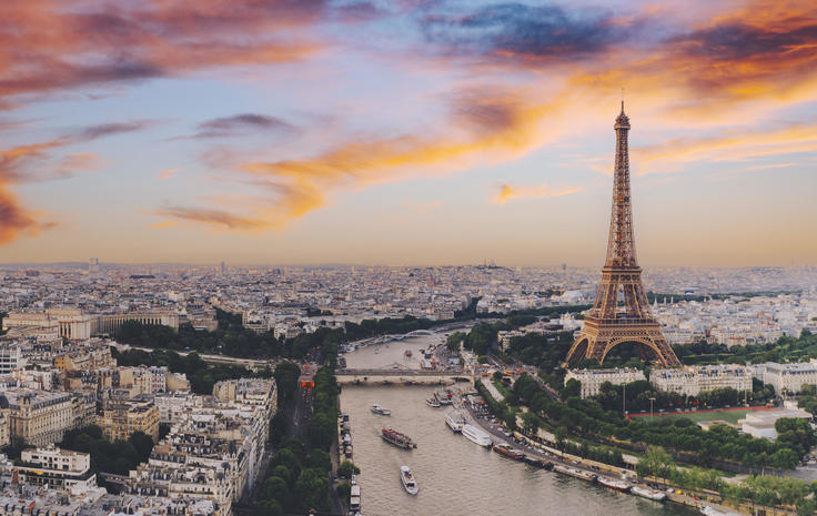 Paris skyline with the Eiffel Tower at sunset, colorful sky, and the Seine River winding through the city.