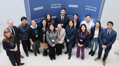 A group of people standing together, smiling, in front of a blue backdrop with text.