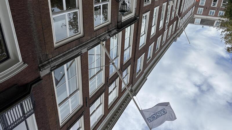Brick building with large windows, view of a cloudy sky, and a flag bearing the word "OSCE"."