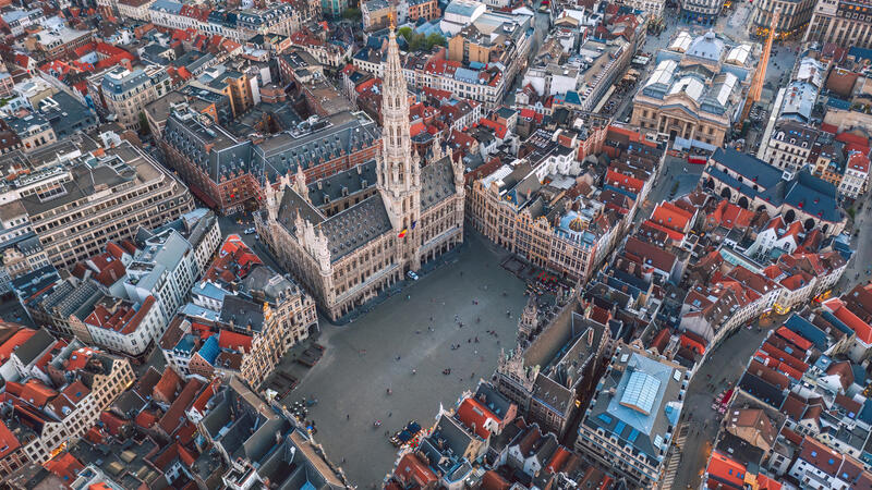 Aerial view of a historic city square surrounded by ornate buildings with a tall spire in the center.
