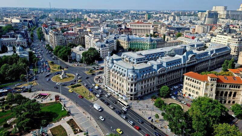 Aerial view of a busy city with classic architecture, green spaces, and a roundabout.